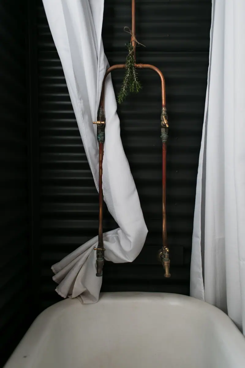 Badkamer met zichtbare koperen leidingen naar een douche